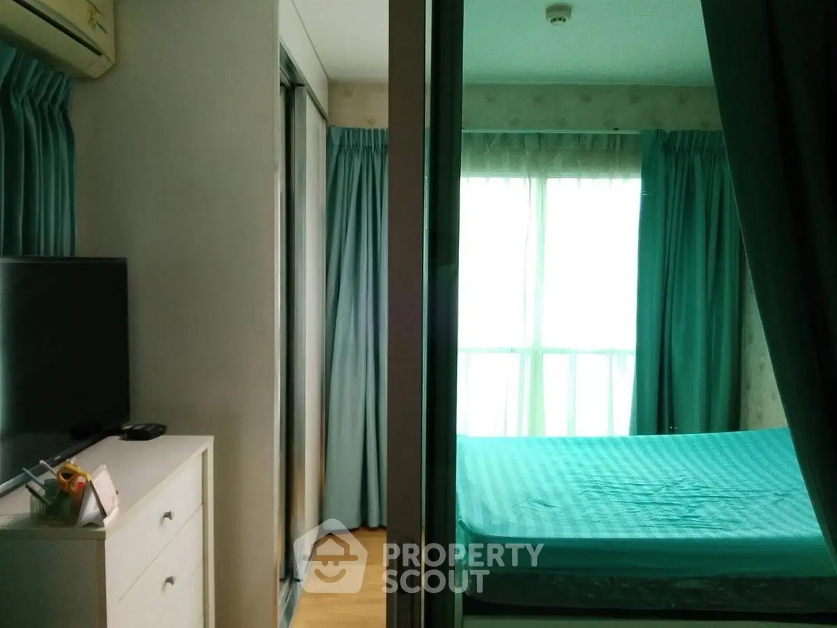 Cozy bedroom with teal curtains and natural light, featuring a TV and dresser for modern living.