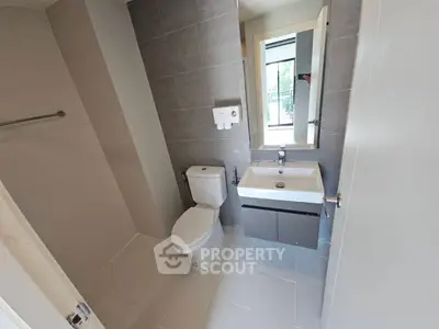Modern bathroom with sleek fixtures and neutral tiles, featuring a large mirror and compact sink.