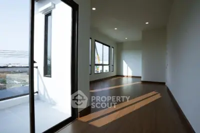 Spacious modern living room with large windows and balcony access, offering abundant natural light and sleek wooden flooring.