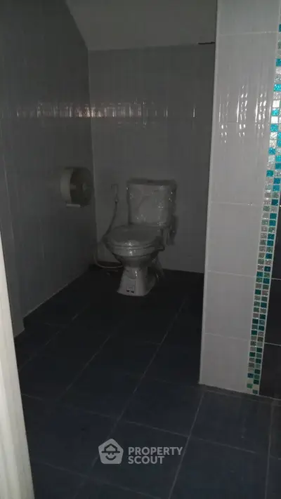 Compact bathroom with tiled walls and floor, featuring a toilet and toilet paper holder.