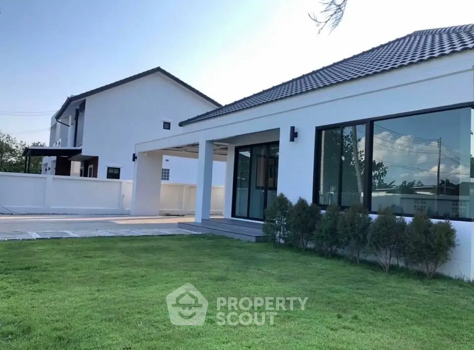 Modern white house with lush green lawn and large windows, showcasing contemporary architecture.