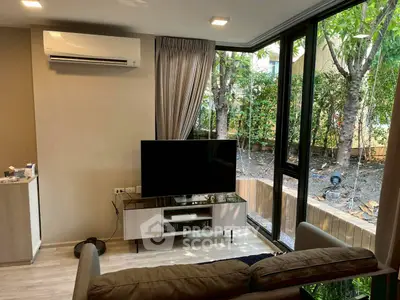 Modern living room with large windows and garden view, featuring sleek furniture and air conditioning.