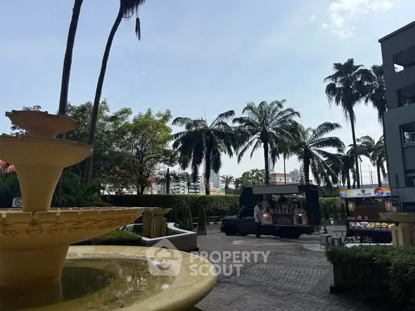 Charming courtyard with fountain and palm trees, featuring a food truck and lush greenery.