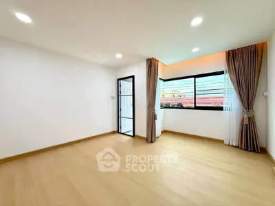 Spacious empty room with large window and wooden flooring, perfect for customization.