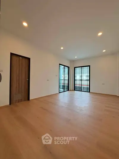 Spacious modern living room with wooden flooring and large windows for natural light.