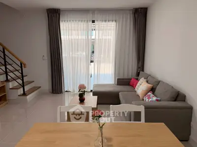 Modern living room with cozy gray sofa and elegant decor, featuring large windows and natural light.