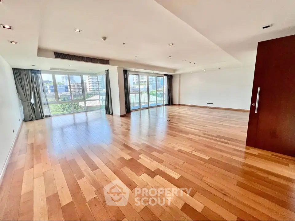 Spacious modern living room with hardwood floors and large windows offering city views.