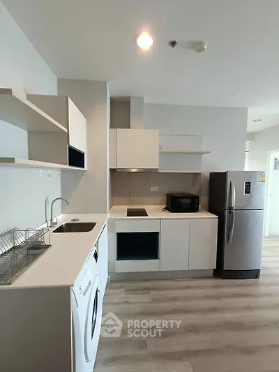 Modern kitchen with sleek appliances and open layout, featuring washing machine and fridge.