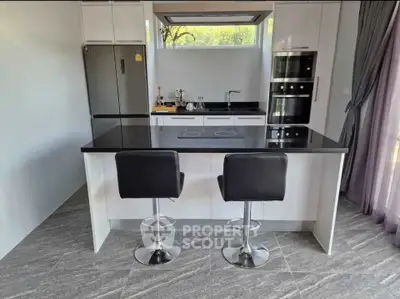 Modern kitchen with sleek black countertops and stylish bar stools, featuring built-in appliances and large window.
