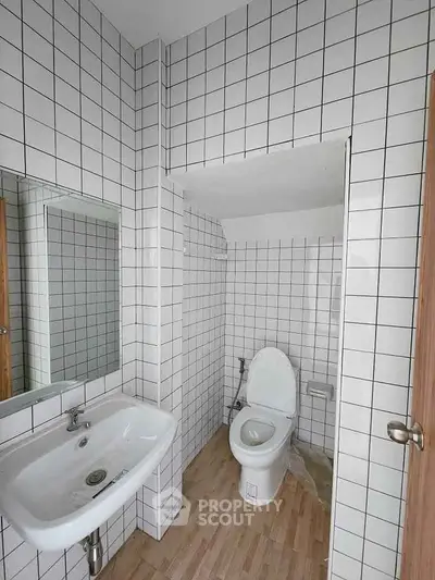 Modern bathroom with white tiled walls and wooden flooring, featuring a sink and toilet.
