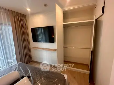 Modern bedroom with open closet and wall-mounted TV, featuring elegant curtains and cozy bedding.
