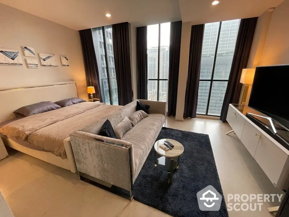 Luxurious bedroom with plush king-sized bed, elegant sofa, and modern entertainment unit, boasting floor-to-ceiling windows with cityscape views.