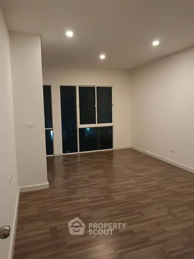 Spacious empty room with wooden flooring and large window, perfect for customization.