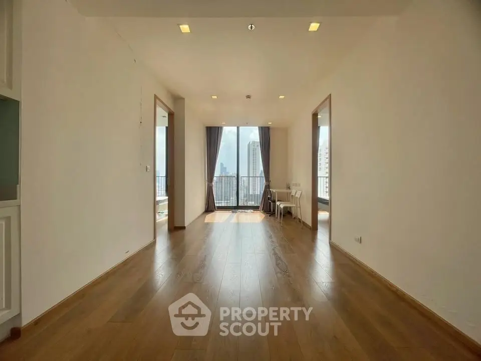 Spacious modern living room with wooden flooring and city view balcony in high-rise apartment.