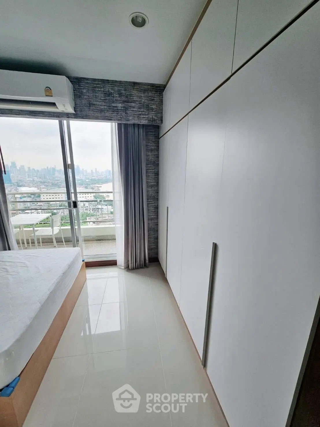 Modern bedroom with city view and large wardrobe in high-rise apartment.