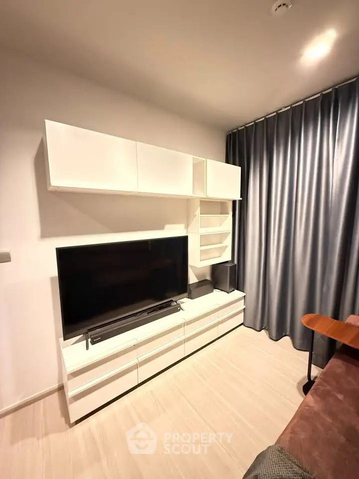 Modern living room with sleek white furniture and large TV, featuring elegant curtains and cozy ambiance.