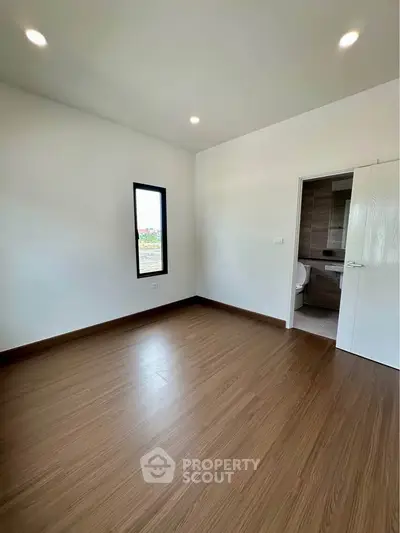 Spacious empty room with wooden flooring and en-suite bathroom, perfect for customization.