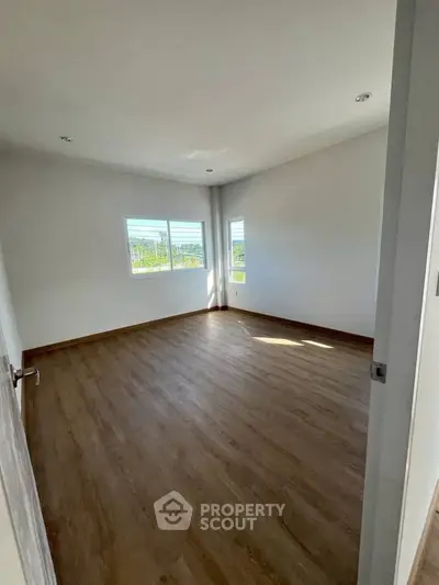 Spacious empty room with wooden flooring and large windows for natural light.