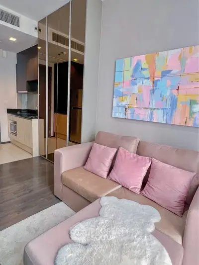 Modern living room with cozy sofa and colorful artwork, adjacent to sleek kitchen area.