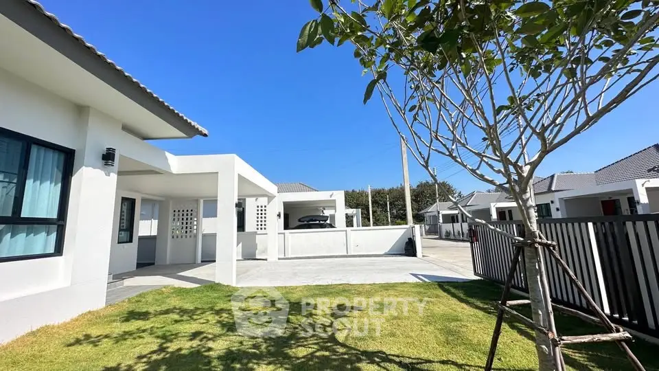 Modern suburban house with spacious driveway and lush green lawn under clear blue sky.