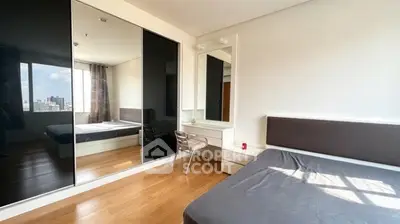 Modern bedroom with mirrored wardrobe and city view, featuring sleek furniture and natural light.