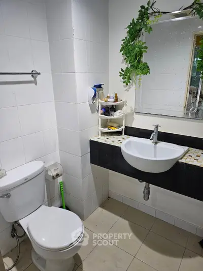 Modern bathroom with sleek sink, toilet, and stylish mirror with greenery accent.