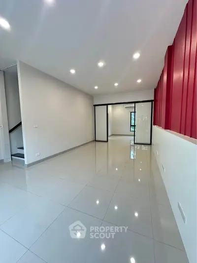 Spacious modern living room with sleek tile flooring and vibrant red accent wall.
