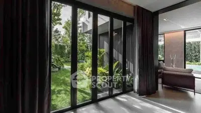 Luxurious living room with floor-to-ceiling windows overlooking a lush garden and pool area.