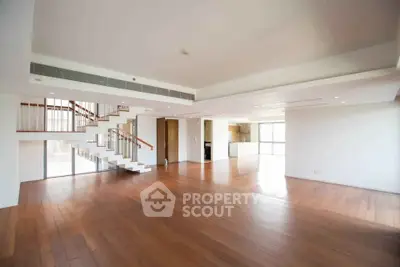 Spacious open-plan living room with wooden flooring and modern staircase