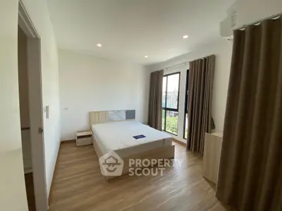 Modern bedroom with large window and wooden flooring in a bright apartment.