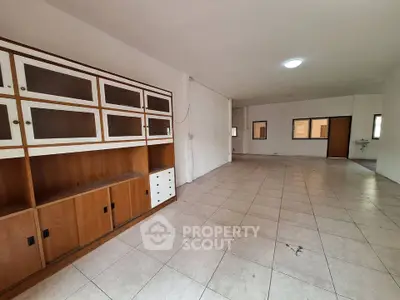Spacious open-plan living area with tiled flooring and built-in wooden cabinets.