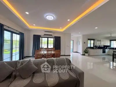 Spacious open-plan living room with modern kitchen and dining area, featuring stylish lighting and large windows.