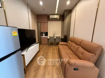 Modern living room with sleek furniture and wooden flooring, featuring a cozy brown sofa and a large TV.