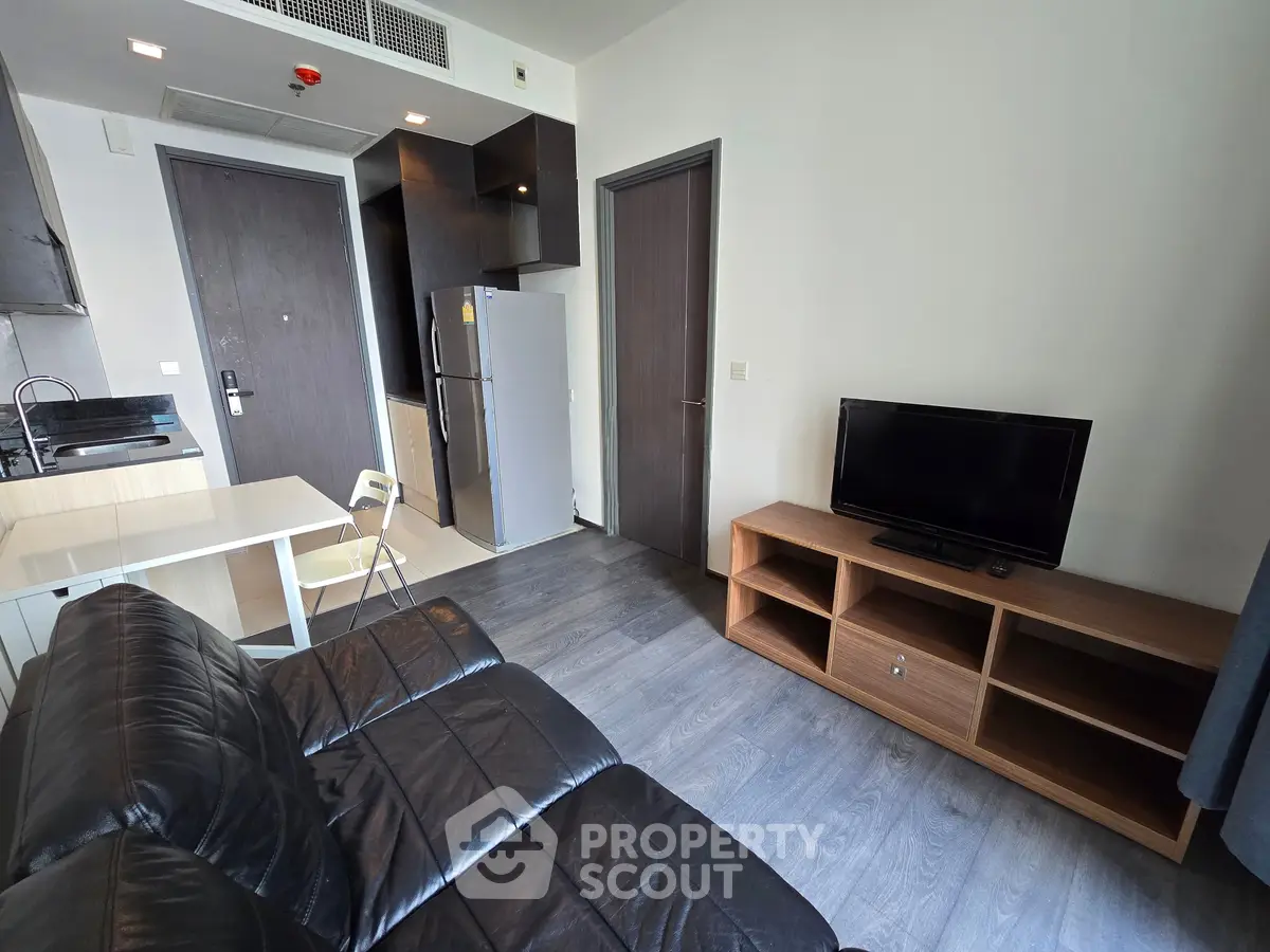 Modern living room with sleek black leather sofa, flat-screen TV, and compact kitchen area.