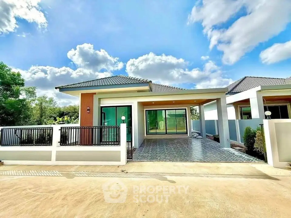Modern single-story house with spacious driveway and lush surroundings under a clear blue sky.