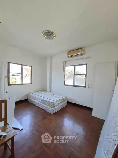 Spacious bedroom with wooden flooring and natural light, featuring a mattress and air conditioning.