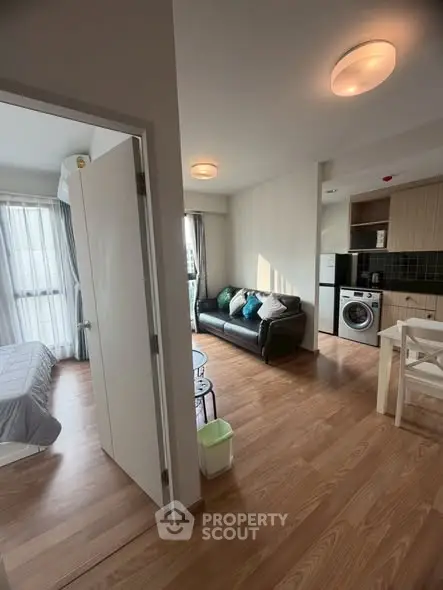Modern apartment interior with open living room and kitchen, featuring wooden flooring and natural light.