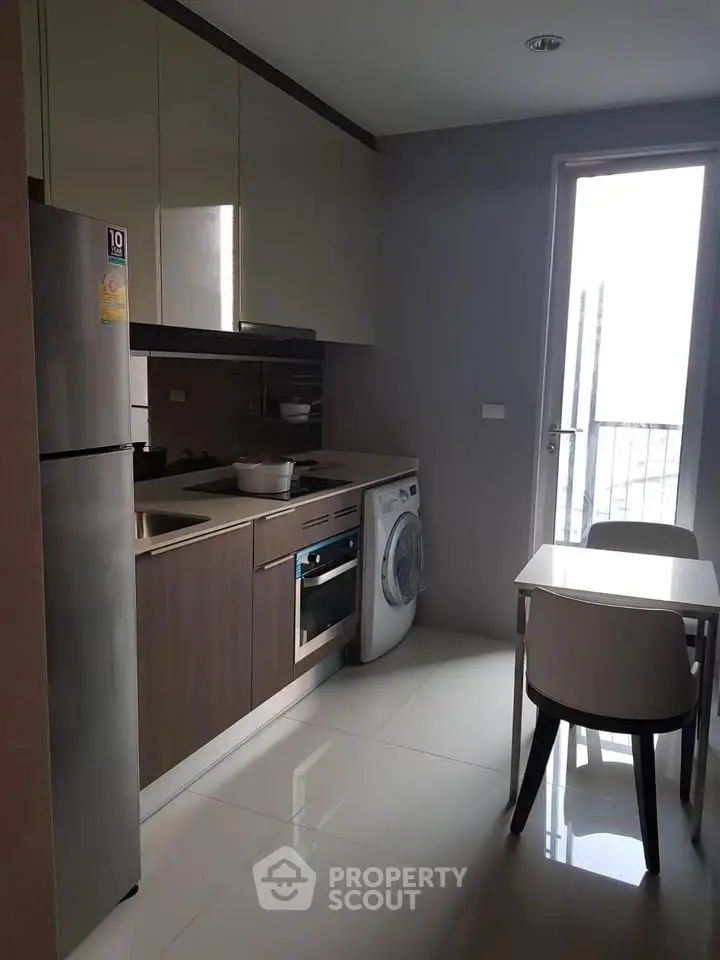 Modern kitchen with sleek cabinets, stainless steel fridge, and compact dining area in a stylish apartment.