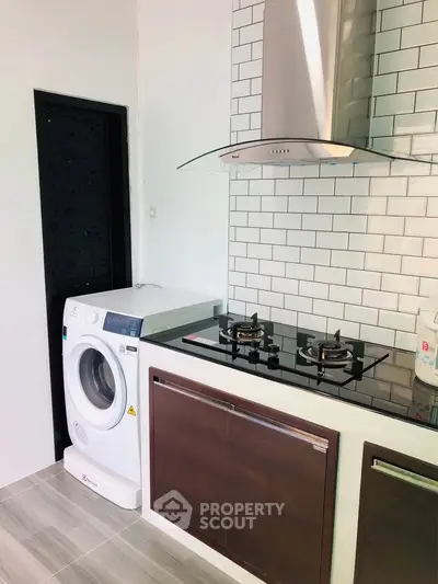 Modern kitchen with gas stove and washing machine in sleek design.