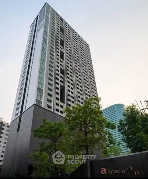 Modern high-rise building with sleek design and lush greenery in urban setting.
