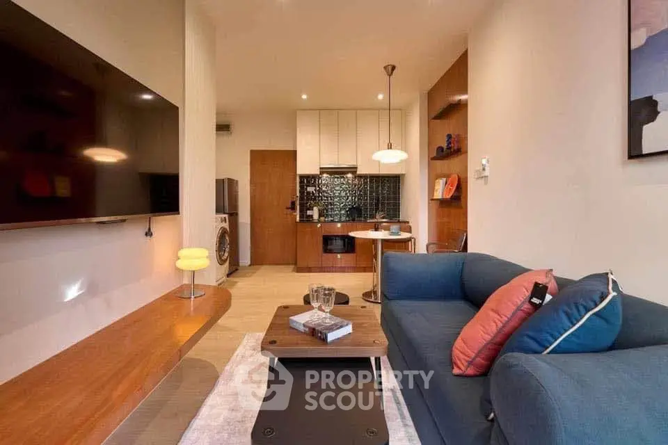 Modern living room with stylish decor and open kitchen layout, featuring a cozy sofa and wall-mounted TV.