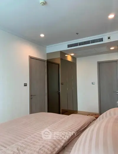 Modern bedroom with sleek design and neutral tones, featuring built-in storage and recessed lighting.