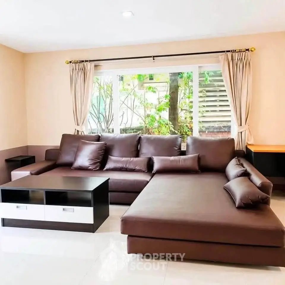 Spacious living room with modern brown sectional sofa and large window view.