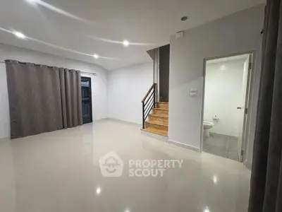 Spacious modern living room with staircase and adjacent bathroom, featuring sleek tile flooring and elegant curtains.