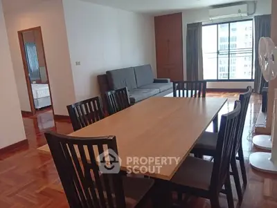 Spacious dining area with wooden table and chairs, adjacent to a cozy living room with a sofa and large window view.