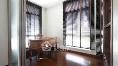 Elegant study room with wooden desk and large windows with blinds, perfect for focused work.