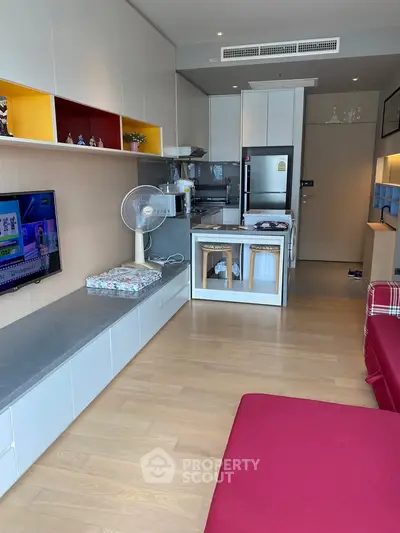 Modern open-layout living room with kitchen, featuring sleek cabinetry and vibrant decor accents.