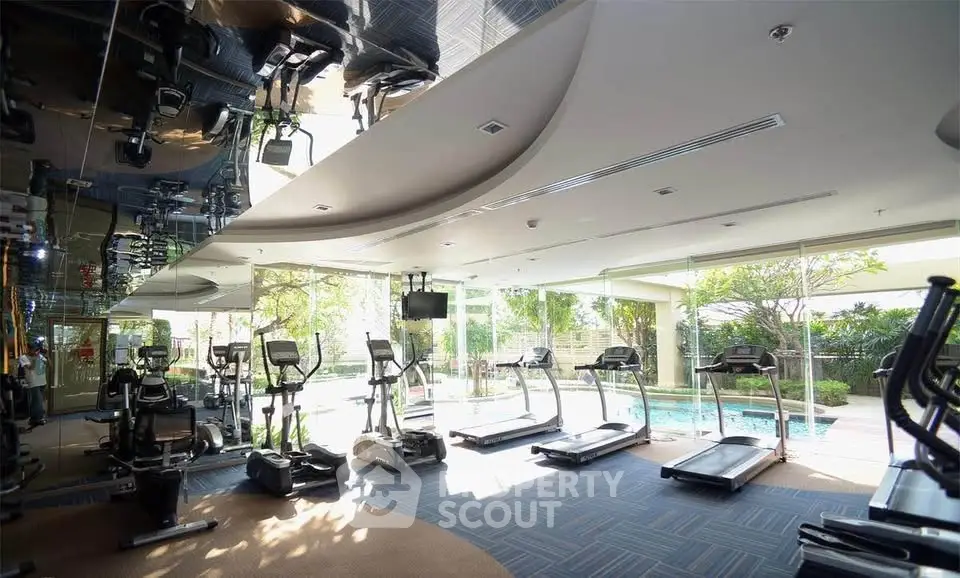 Spacious gym with modern equipment and pool view in luxury residential complex.