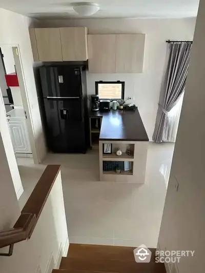 Modern kitchen with sleek black fridge and island, featuring open layout and natural light.