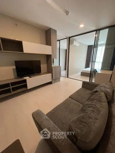 Modern living room with sleek furniture and glass partition leading to bedroom.